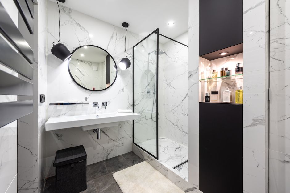 Shower room against washbasin and mirror between shiny lights in bathroom with assorted perfume in bottles on shelves