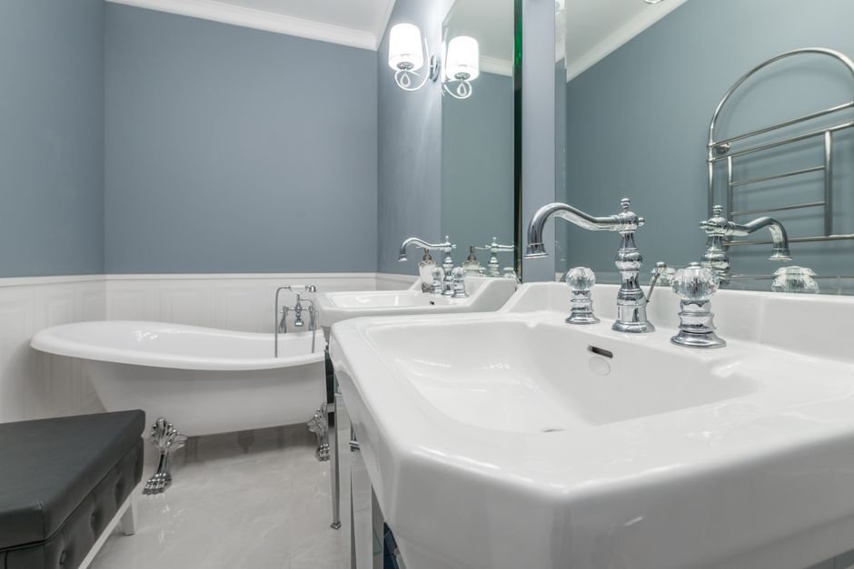 White sinks with stylish faucets against bathtub placed in light bathroom in modern apartment