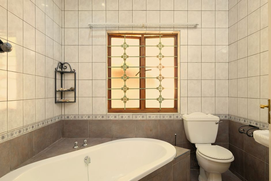 Elegant bathroom featuring a bathtub, toilet, and window with tiled walls.