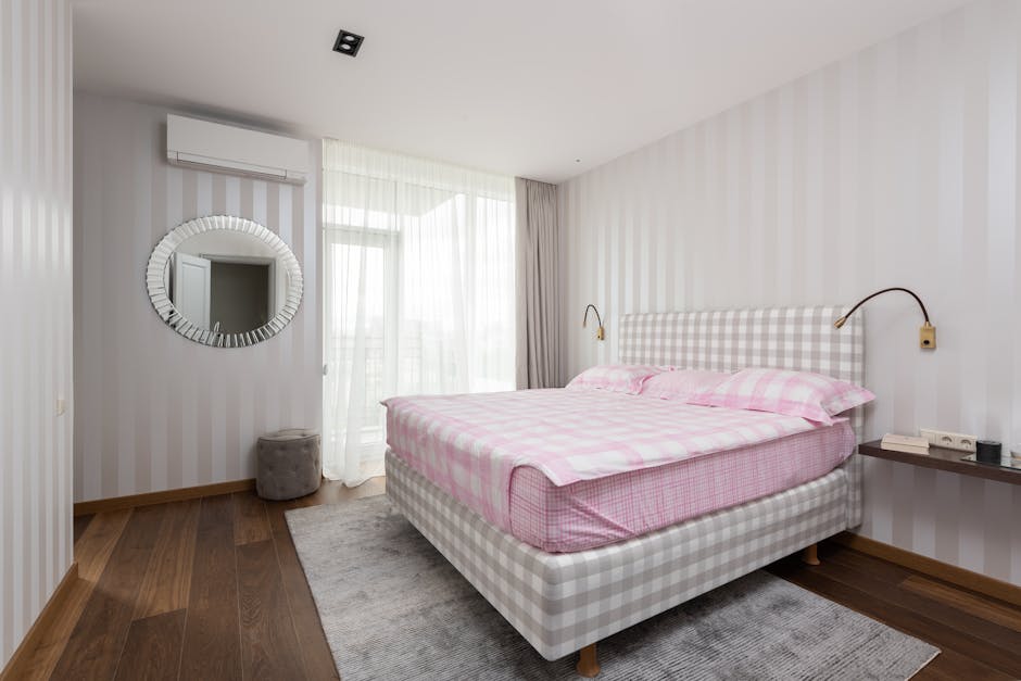 Comfortable bed with pink linen placed on carpet in spacious bedroom with light walls in daytime