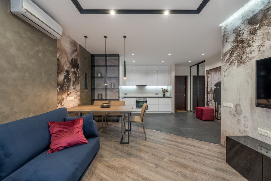 Cozy sofa with cushions placed in front of TV hanging above cabinet in contemporary studio apartment with dining and kitchen zones
