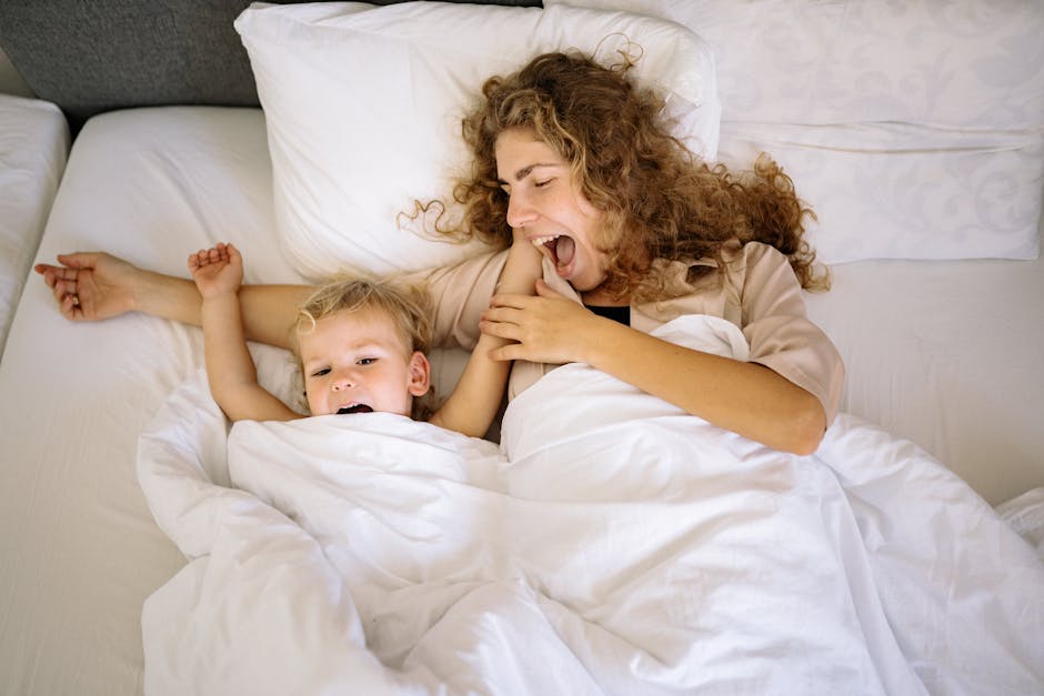 Happy mother and son bonding in bed, sharing a joyful morning moment under white blankets.