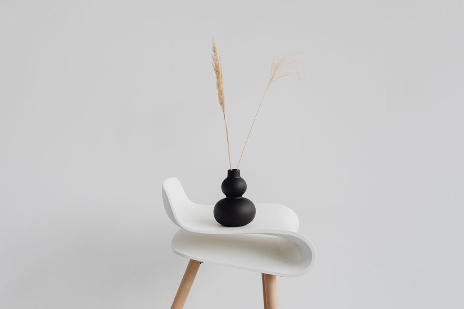 A sleek black vase with wheat ears on a modern white chair against a minimal background.