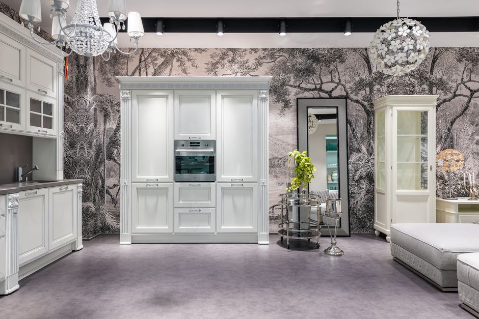 White cabinets with modern appliances placed in spacious kitchen with green plant and comfortable seats near decorative elements in apartment