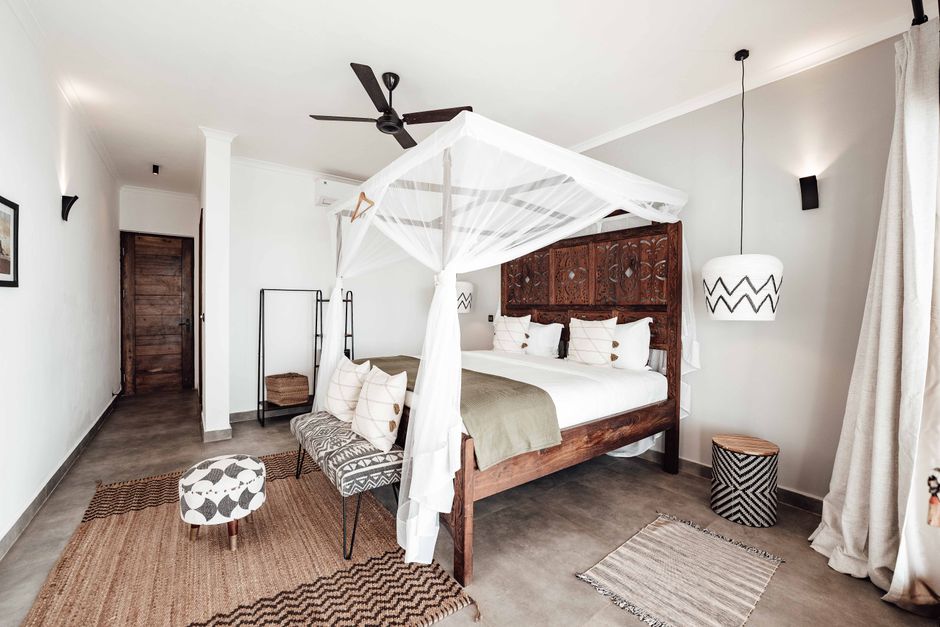 A stylish bedroom featuring a carved wooden four-poster bed, modern lighting, and cozy textiles.