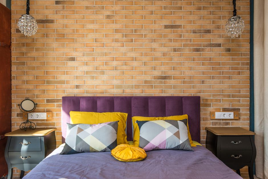 Contemporary bedroom decor with a brick wall and vibrant pillows.