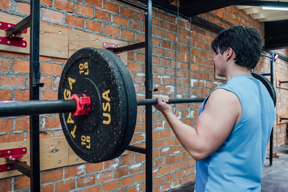 An adult male lifting weights on a barbell in a gym setting with brick walls in Mexico City.