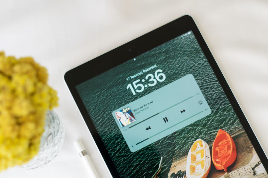 Top view of a tablet displaying a music app, with a yellow flower bouquet nearby on a white surface.