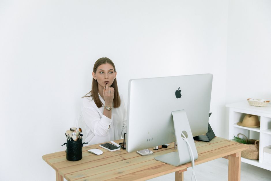 Woman applying makeup at desk, balancing work and beauty routine indoors.