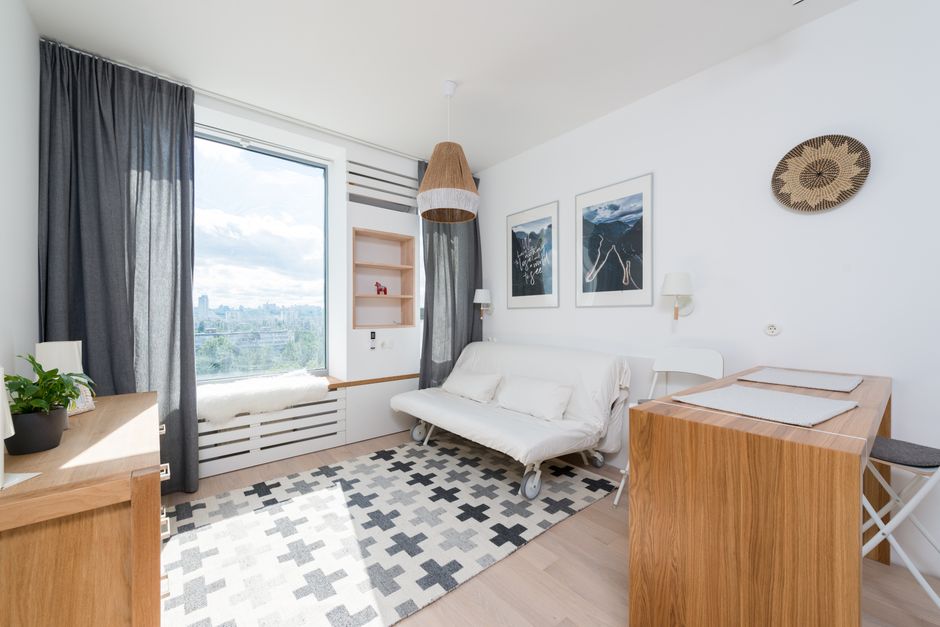 Comfortable sofa placed on rug at wall decorated with paintings in modern room with wooden table and drawer near window