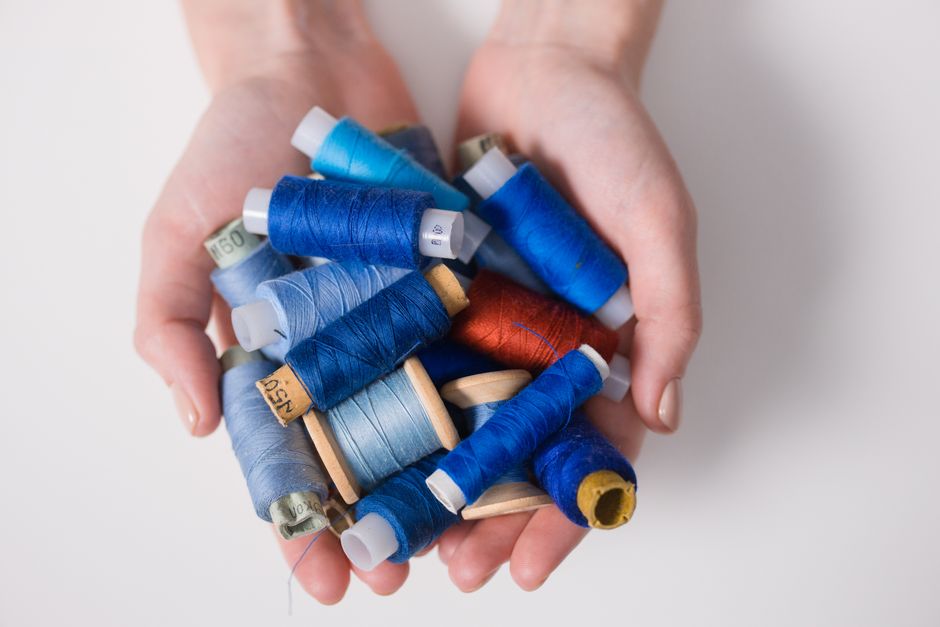 Hands holding colorful sewing threads on a white surface, embodying creativity and craftsm