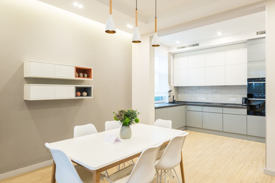 Table with chairs placed near kitchen counter with white and gray cabinets near modern appliances in stylish spacious apartment with decorations