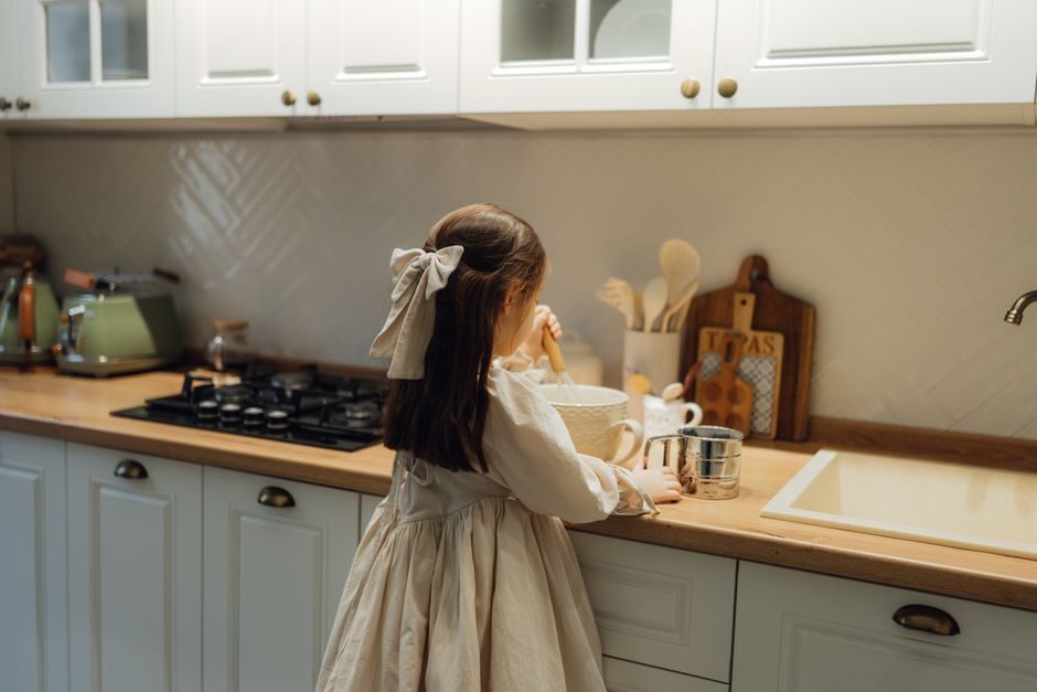 A young girl preparing a meal in a warm, modern kitchen setting.