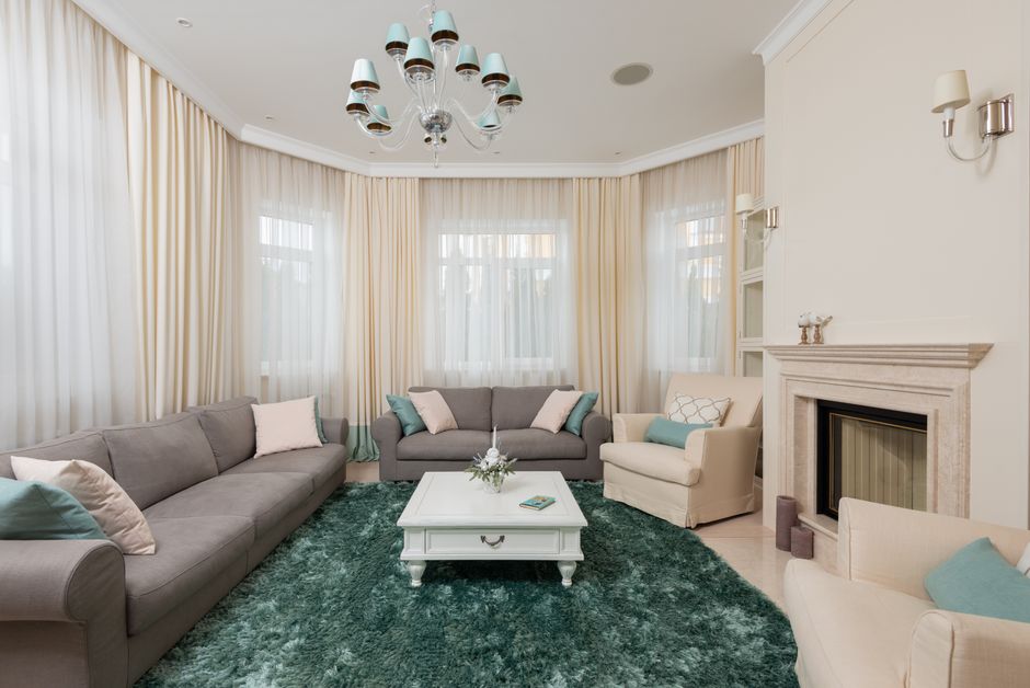 Interior of classic living room with gray sofas and beige armchair on soft carpet near stone fireplace under chandelier