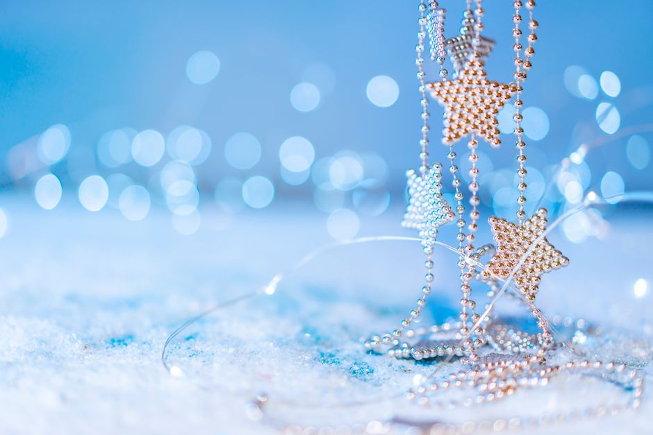 Close-up of silver star decorations on snow with vibrant bokeh lights.