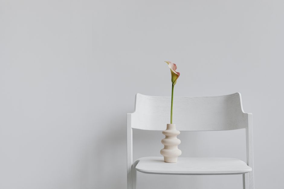 A single calla lily in a decorative vase atop a white chair, showcasing minimalist elegance.