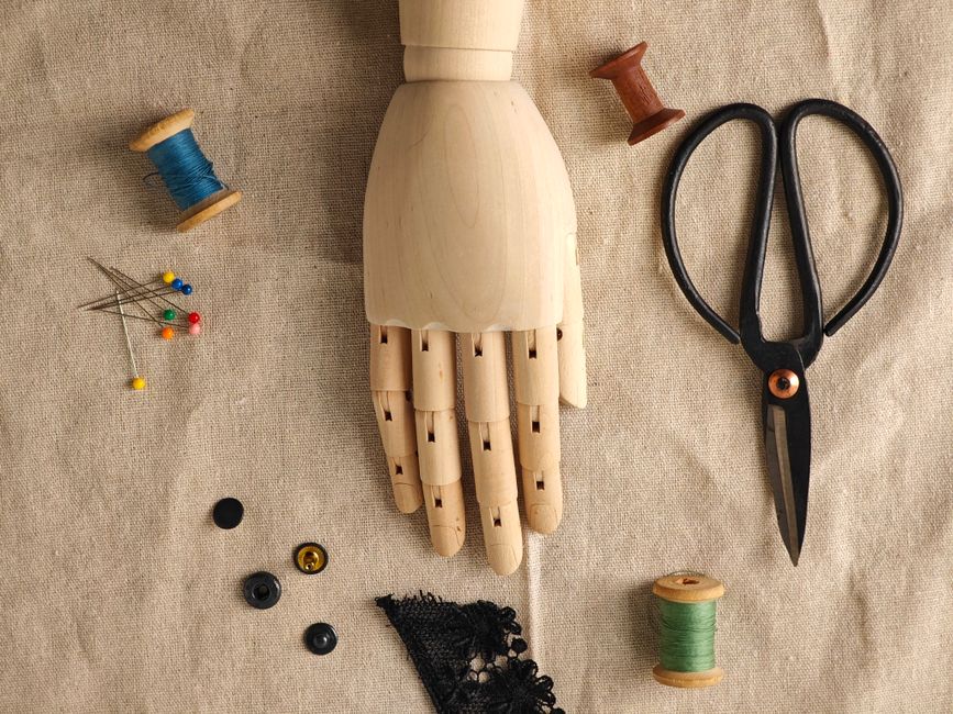 Flat lay of sewing tools and wooden mannequin hand on linen fabric.