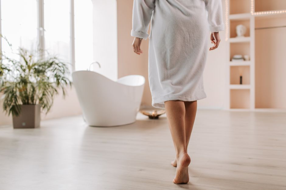 A person in a bathrobe walks towards a stylish bathtub in a bright, modern bathroom.