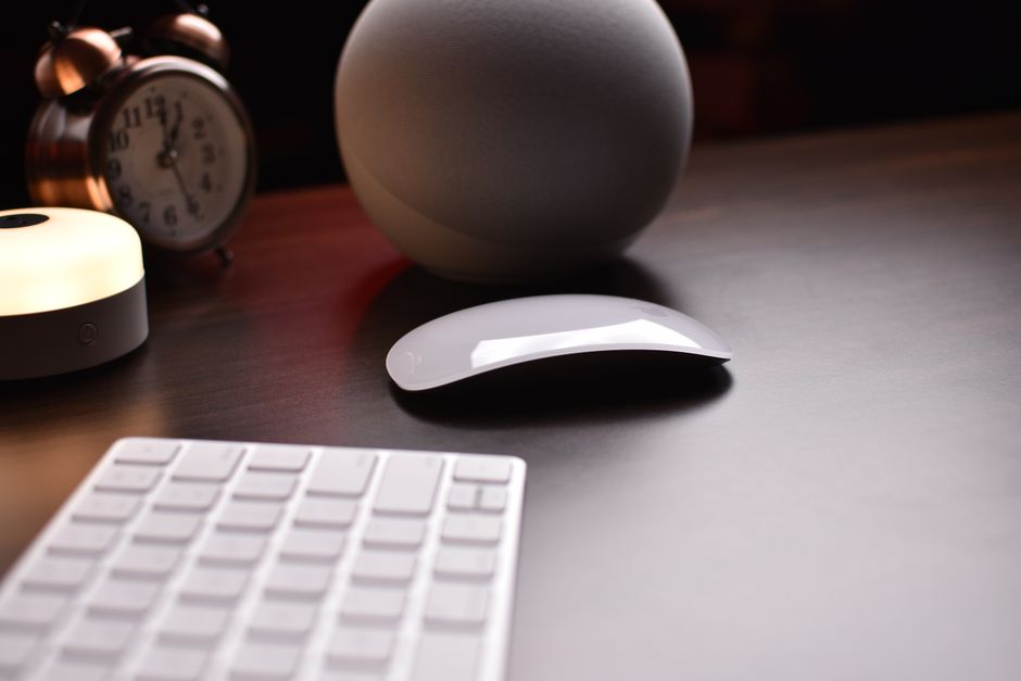 Close-up of a sleek wireless mouse and keyboard on a wooden desk with soft lighting.
