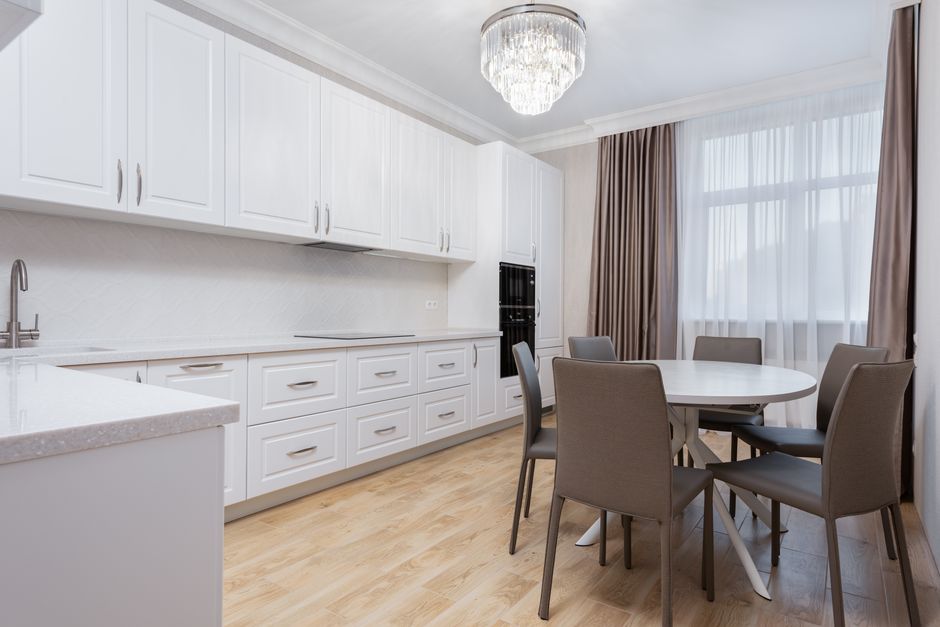 White cabinets against round shaped table with chairs on parquet under shiny lamp in house