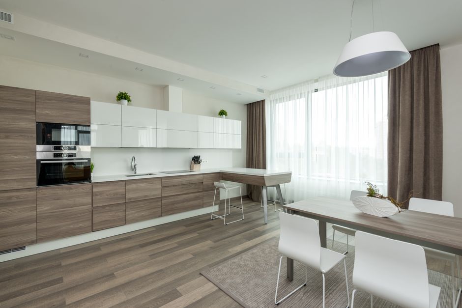 Interior of modern kitchen with cabinets in white and wooden design and dining room with table and chairs placed in middle of room