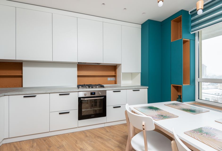 Modern cabinet with gas stove and oven against table with placemats under light bulbs in apartment