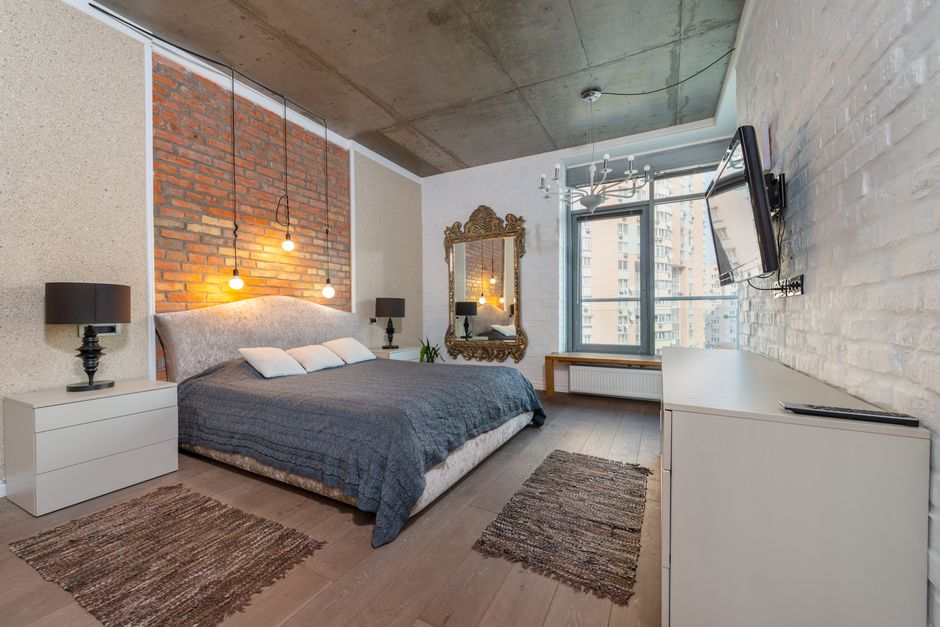 Spacious industrial-style bedroom with brick wall, cozy bed, and modern decor.