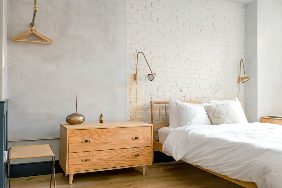 Bright minimalist bedroom interior featuring a wooden bed, drawers, and unique wall lamps.