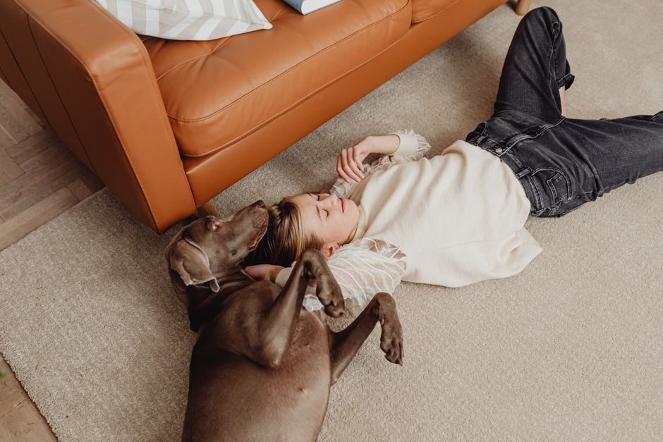 Young girl enjoying a playful moment with her dog on a carpeted floor.