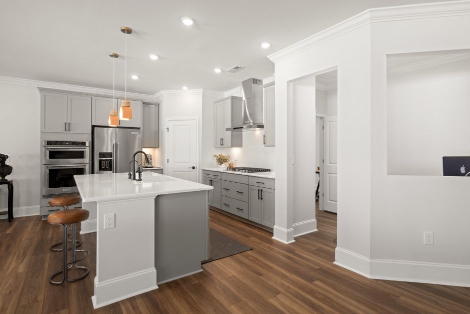 Spacious modern kitchen interior with grey cabinets, island, and barstools.