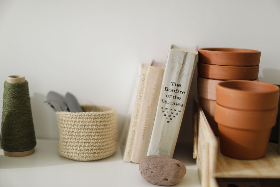 Still life of crafting tools and books on a shelf with terracotta pots and thread.