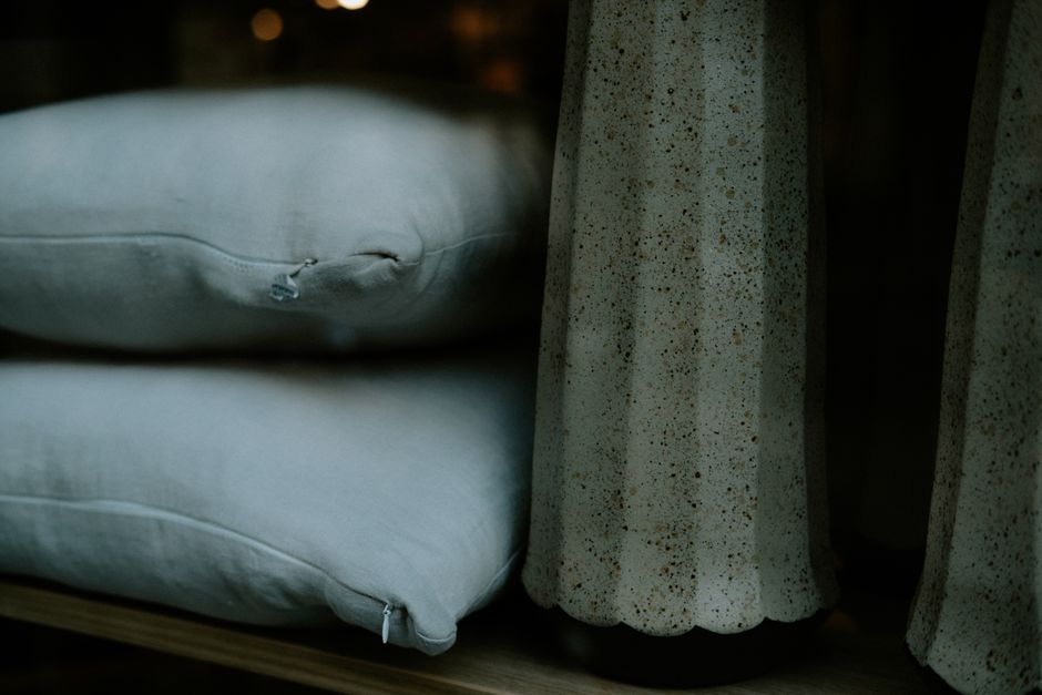 Close-up of stone vases and stacked cushions on a wooden shelf, showcasing minimalist interior design.