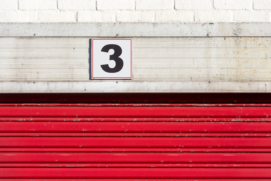 Close-up of a red garage door with a large number three sign above it.