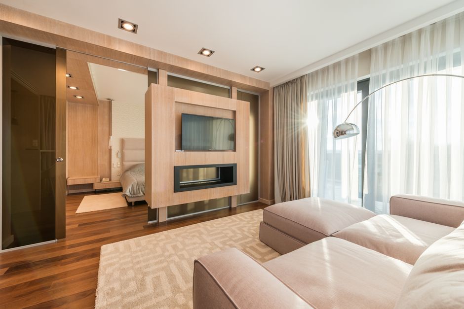 Comfortable couch located on rug near window with curtains against modern TV in light modern apartment with bed in bedroom